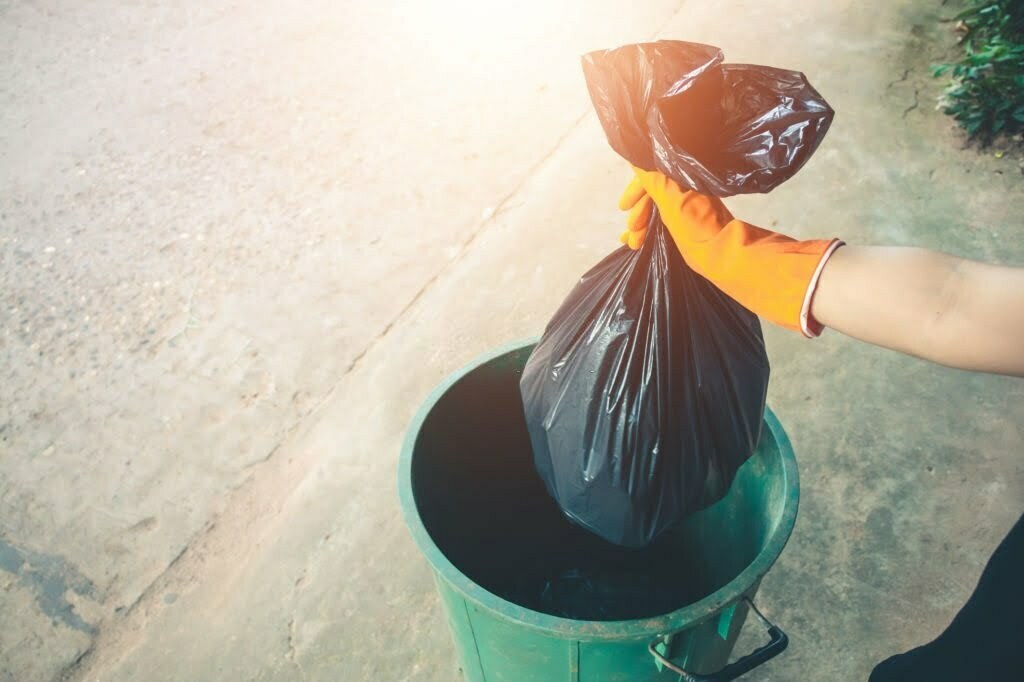 Close-Up Of Woman Putting Garbage Bag In Plastic Container